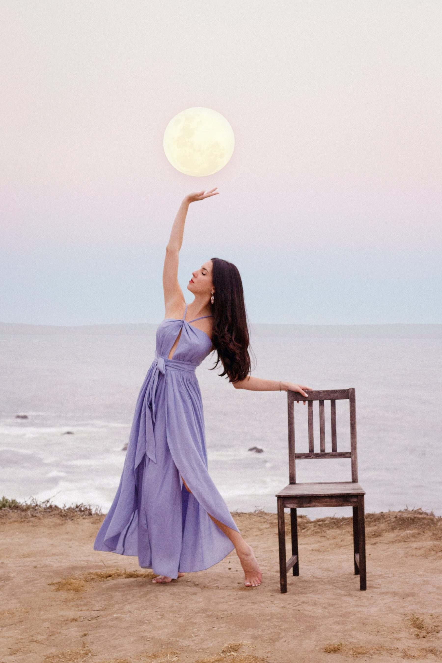 Caro Rodriguez on the beach at dusk, reaching toward the full moon