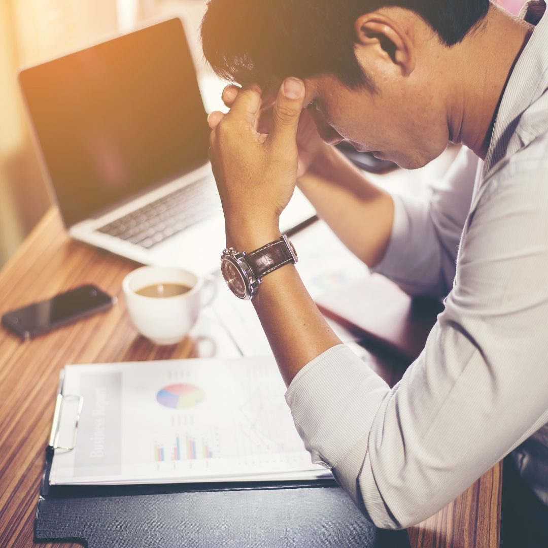 Man at his desk holding his head, feeling overwhelmed