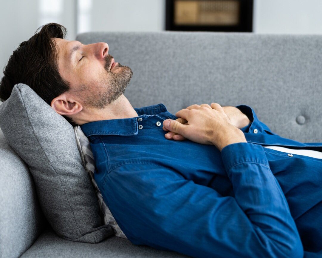 Man resting with eyes closed on a sofa, hands on his chest
